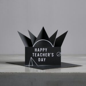 Handmade pop-up card featuring angular folds and sans-serif white text, set on a smooth concrete surface