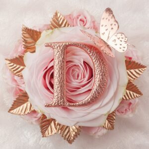 The 'D' glimmers in rose gold, accompanied by roses and a butterfly, set against a dreamy background