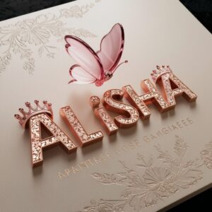 A luxurious 3D 'Alisha' logo in rose-gold letters with floral crowns and a hovering pink glass butterfly