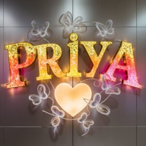 Golden Priya text with an orange-to-pink gradient, neon highlights, and a whimsical butterfly."